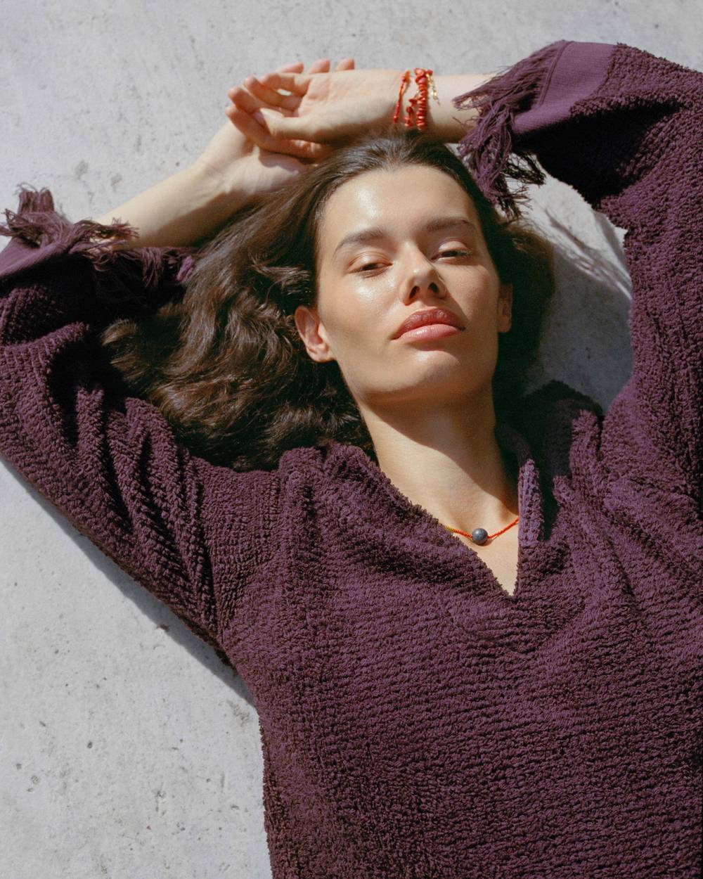 A woman sitting on the floor next to a glass-table with the light seeping in creating a shadows all around. She is wearing a cream and sand printed collared shirt and matching shorts.