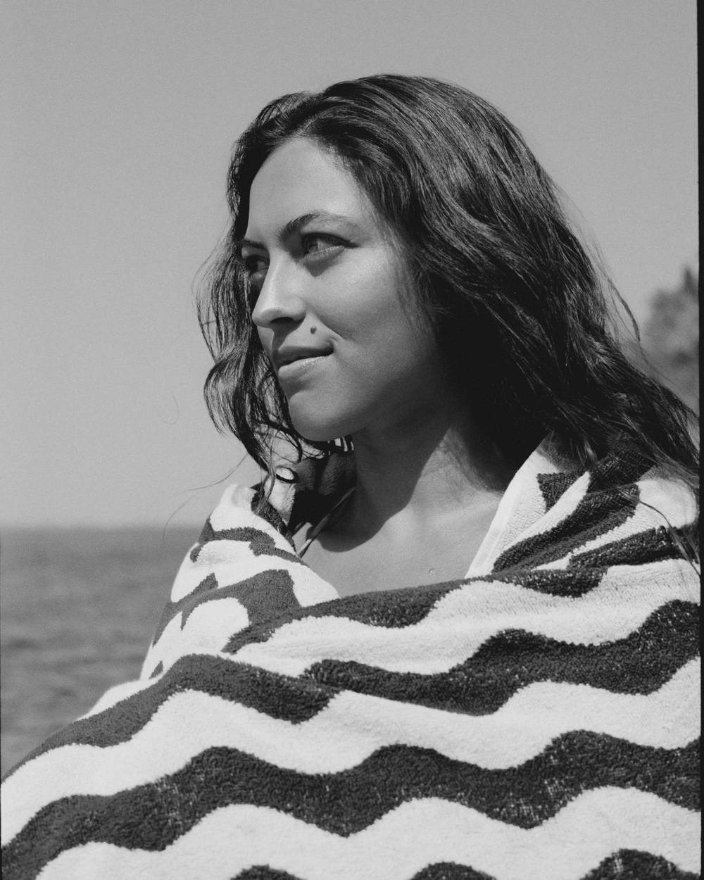 A blue and white towel hanging on a chair on a cobblestone beach. In the background you can see similar red chairs standing around.