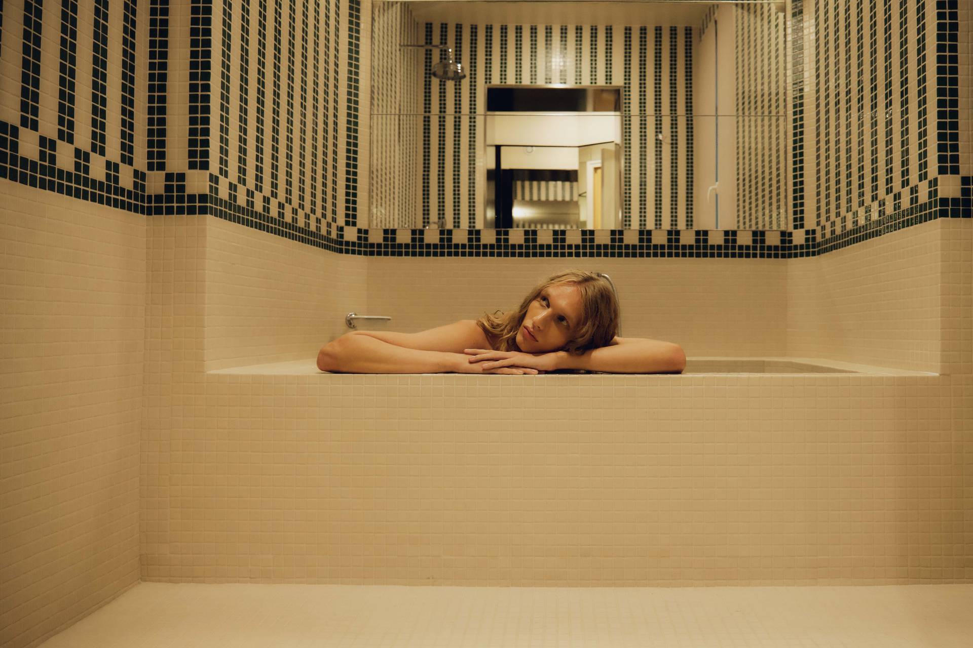 A model sitting on the edge of a luxurious bathtub in a tiled bathroom, wearing a terracotta bathrobe, capturing a blend of indulgence and modern design.