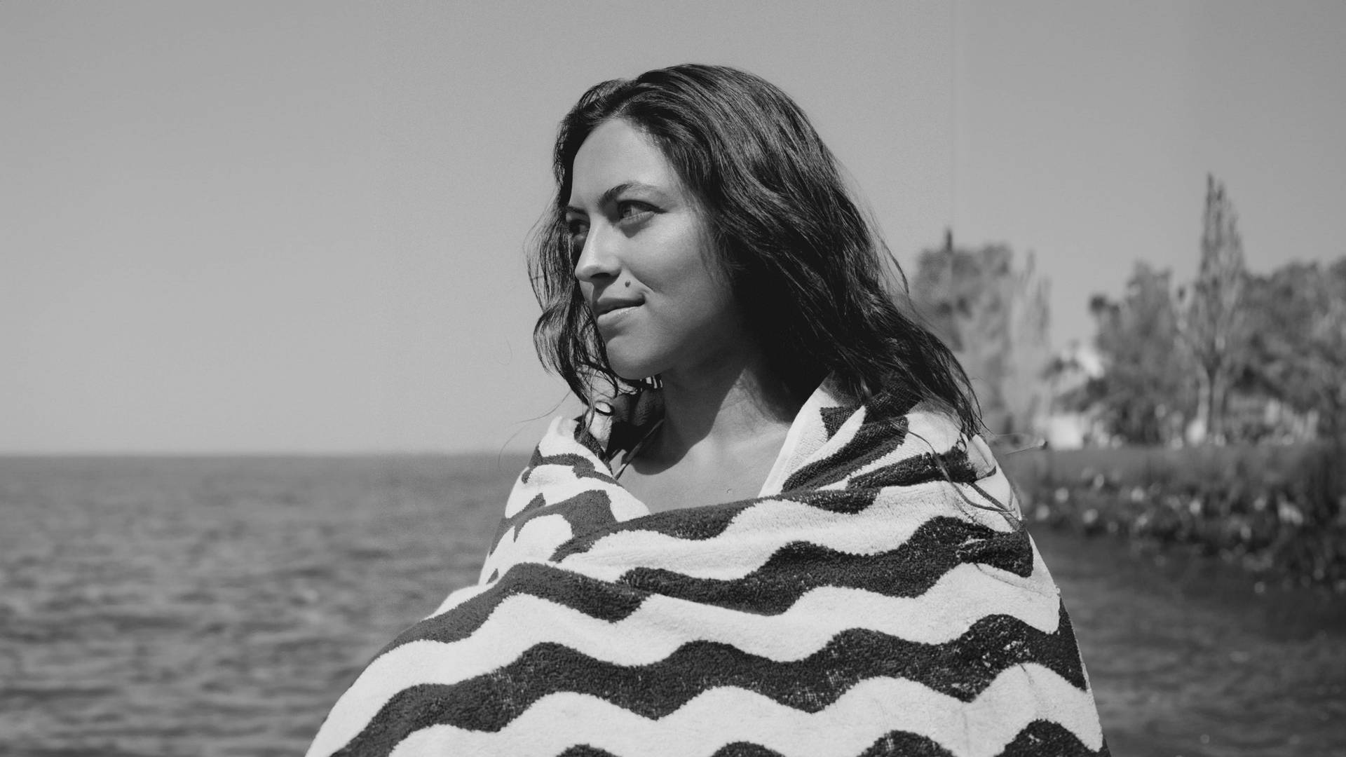 A blue and white towel hanging on a chair on a cobblestone beach. In the background you can see similar red chairs standing around.