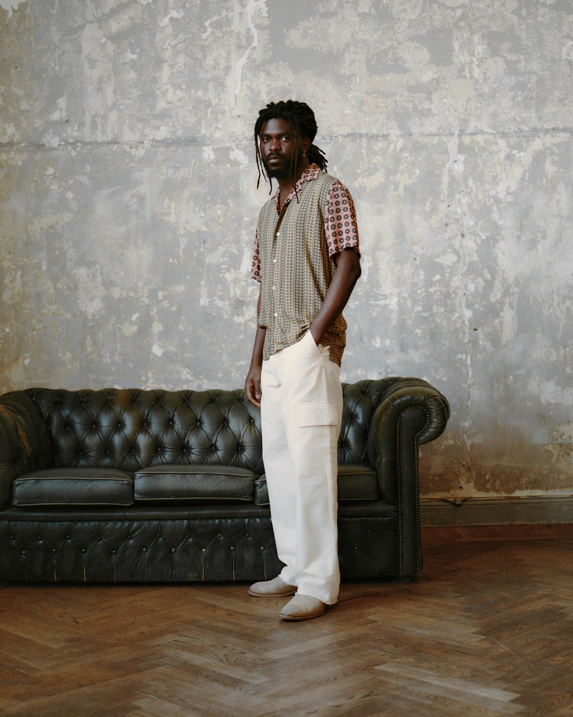 Model in a mixed-print short-sleeve shirt, and ivory cargo trousers against a textured wall.