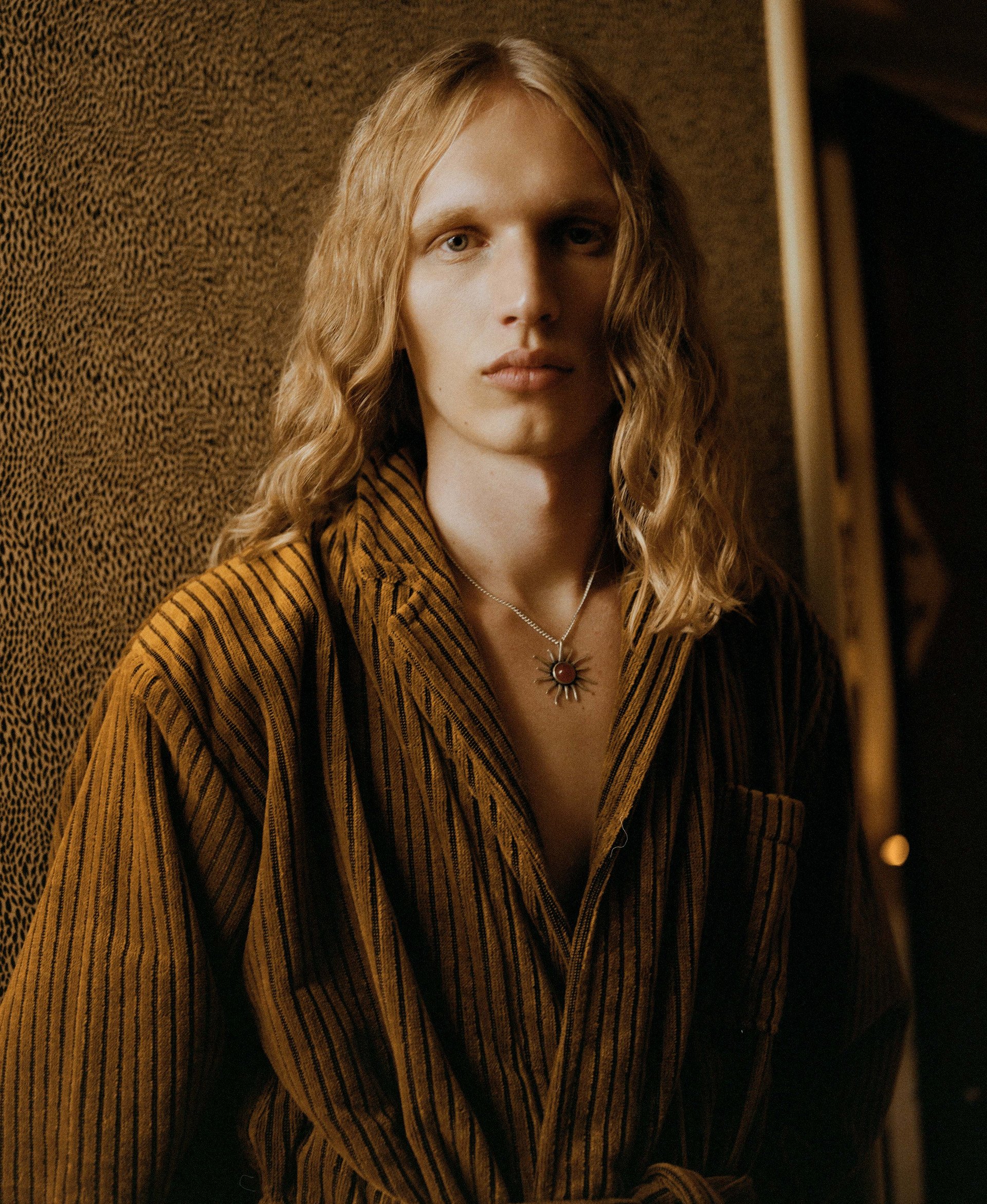 A model in a striped mustard robe, accessorized with a statement necklace, emphasizing artistic textures and fashion-forward layering.